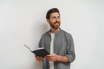Smiling man in casual clothes standing with open notepad and looking at side white background
