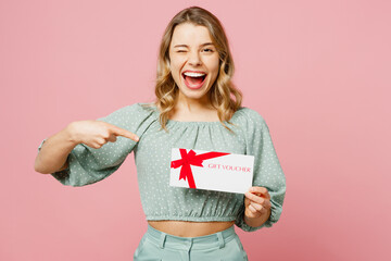 Young shocked happy woman wear casual clothes hold point finger on gift certificate coupon voucher card for store wink isolated on plain pastel light pink background studio portrait Lifestyle concept