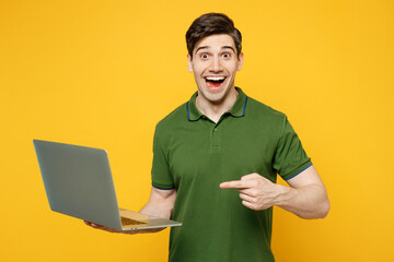 Shocked young surprised happy IT man wears green t-shirt casual clothes hold use work point index...
