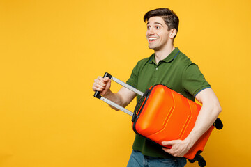 Traveler amazed fun man wear green casual clothes hold suitcase look aside isolated on plain yellow background. Tourist travel abroad in free spare time rest getaway. Air flight trip journey concept.