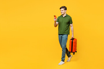 Fototapeta na wymiar Traveler happy man wear green casual clothes hold suitcase mobile cell phone isolated on plain yellow background Tourist travel abroad in free spare time rest getaway. Air flight trip journey concept.