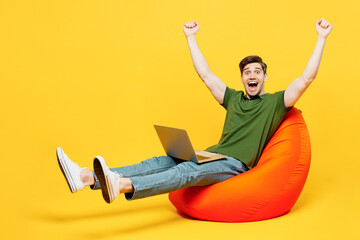 Full body young happy IT man he wears green t-shirt casual clothes sit in bag chair hold use work...