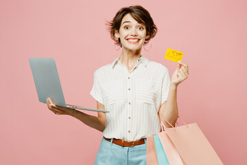 Young woman wear casual clothes hold package bags using laptop pc computer, credit bank card do online shopping isolated on plain light pink color background studio. Black Friday sale buy day concept.