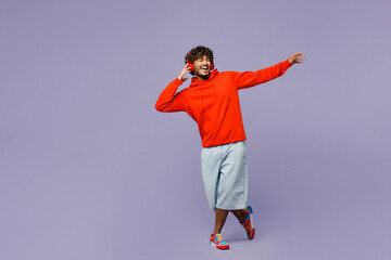 Full body smiling fun young Indian man wear red orange hoody casual clothes listen to music in...
