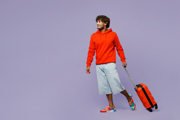 Traveler young Indian man wears casual clothes hold bag walk isolated on plain pastel purple...
