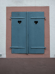 Window with blue closed wooden shutters on white stone wall background.