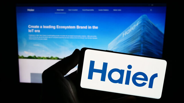 Stuttgart, Germany - 08-17-2023: Person holding smartphone with logo of home appliances company Haier Group Corporation on screen in front of website. Focus on phone display.