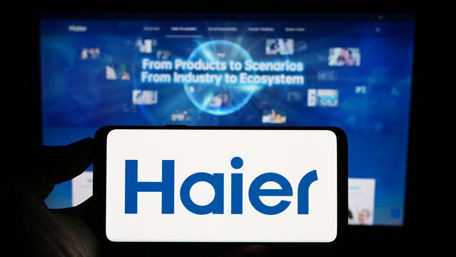 Stuttgart, Germany - 08-17-2023: Person holding cellphone with logo of home appliances company Haier Group Corporation on screen in front of webpage. Focus on phone display.