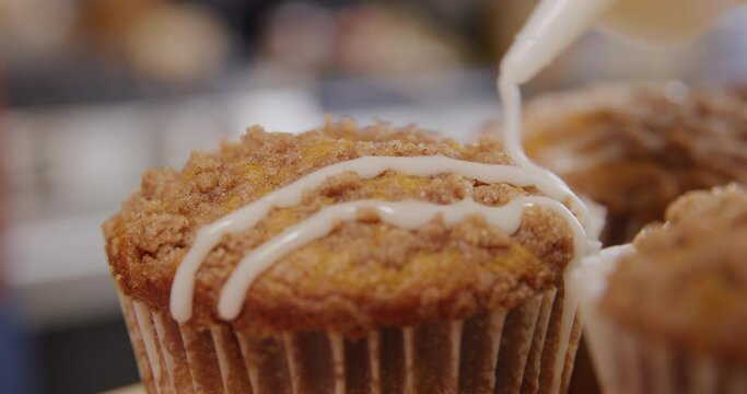 Drizzling white glaze over pumpkin spice muffins closeup