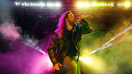 Rock and roll concert. Artistic, expressive man with long hair, in leather clothes making...