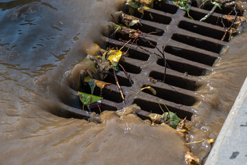 Dirty rainwater flowing into a metal grate on the road.