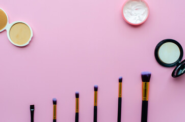 set makeup brushes and cosmetics on pink or purple colored background. Top view. copy space