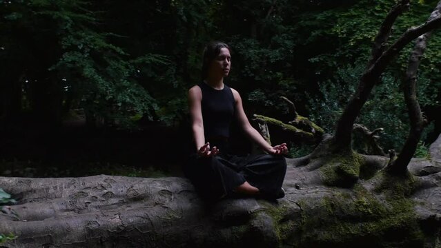 Calm zen moment of young woman meditating in verdant clearing, slowmo