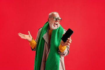 Portrait of funny senior man who laughing because of win dressed trendy, stylishly holding phone in his hands with blank screen.