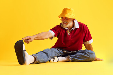 Body size view of attractive cheerful funny man sitting on floor and having fun isolated over bright yellow color background