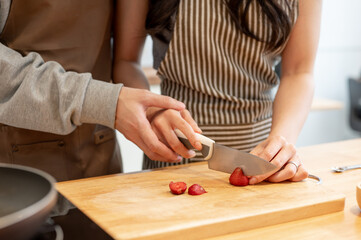 Cropped image of a man teaching and helping his girlfriend cut strawberries on a chopping board