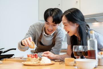 A handsome Asian man is pouring syrup on pancakes, enjoys cooking pancakes with his girlfriend