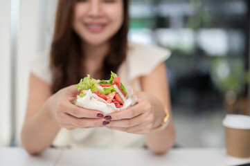 Close-up image of a businesswoman holding a sandwich, eating a sandwich at her desk