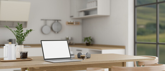 Close-up image of a laptop mockup on a wooden dining table in a minimalist, Scandinavian kitchen.