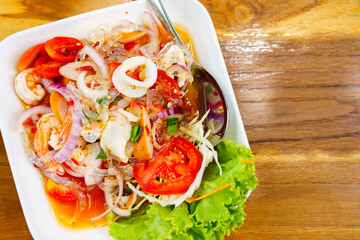 Seafood salad in a white plate placed on a wooden table, top view, a spicy Thai dish.