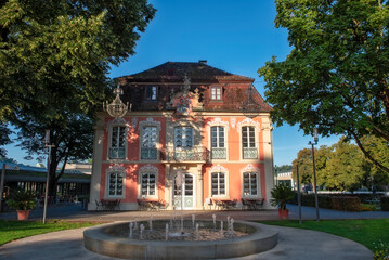 Die Westfassade des Rokokoschlösschens im Stadtpark von Schwäbisch Gmünd im morgendlichen Sonnenlicht, mit Brunnen und menschenleerem Außenbereich