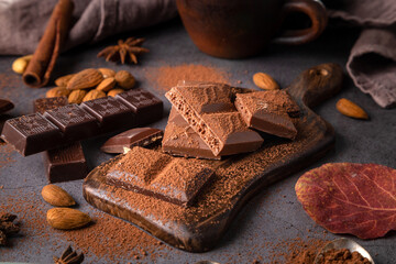 Pieces of chocolate and nuts on a plank on a dark background