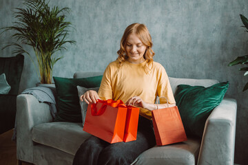 Cheerful happy shopaholic woman with lots of shopping bags, she is sitting on an sofa and celebrating at home. High quality photo