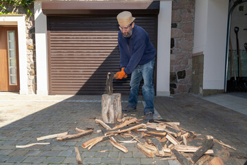 Man with glasses chopping wood in front of garage door.