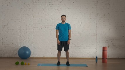 Man fitness coach in sportswear doing a warm up for online class at his home studio.