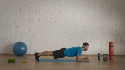 Man fitness trainer in sportswear doing static plank for online class at the home studio.