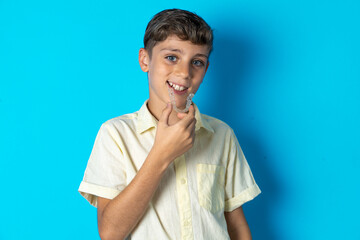 Beautiful kid boy wearing casual shirt holding an invisible aligner ready to use it. Dental healthcare and confidence concept.
