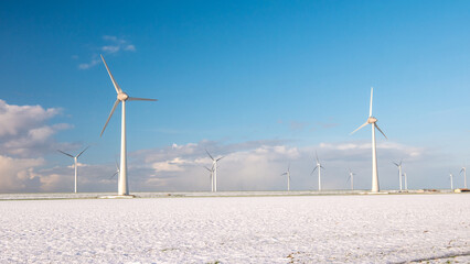 windmill park with snow during winter and a blue sky, windmill park in the ocean aerial view with wind turbine Flevoland Netherlands Ijsselmeer. Green energy 