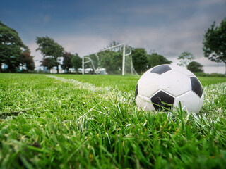 Classic soccer of foot ball on freshly cut grass, goal post in the background. Preparation for new season or game theme. Dramatic sky, selective focus. Nobody. Popular outdoor activity. © mark_gusev