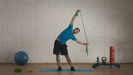 Man fitness coach in sportswear doing side body bends with rubber band exercise.