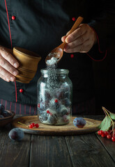 Adding sugar to a jar of plums. Preparing a sweet drink from fresh plum and sugar on the kitchen table. The process of preserving berries in a jar