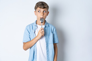 Very hungry Beautiful kid boy wearing  casual clothes holding spoon into mouth dream of tasty meal