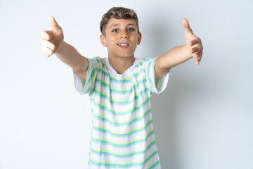 Beautiful kid boy wearing striped casual t-shirt looking at the camera smiling with open arms for hug. Cheerful expression embracing happiness.