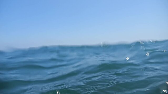 Under and over the sea: a slow-motion dive and emergence amidst gentle waves on a sunny day.