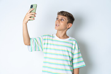 Beautiful kid boy wearing striped casual t-shirt smiling and taking a selfie ready to post it on...