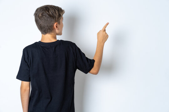 Beautiful kid boy wearing black casual t-shirt pointing to object on copy space, rear view. Turn your back