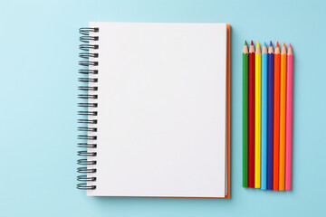 Top view of empty notebook with colorful crayon pencils on pastel blue background