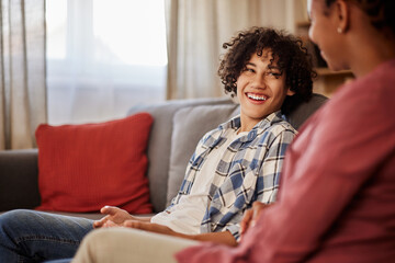 A smiling African-American teenage boy in a plaid shirt and jeans talking with his mother. © bnenin