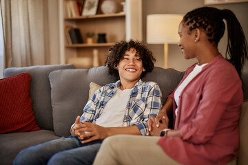 A smiling teenage boy sitting on the couch with his mother, making jokes.