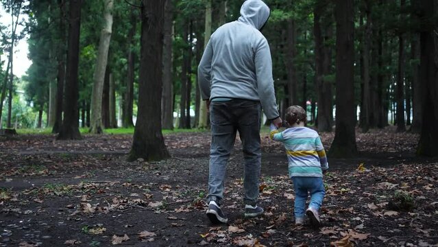 a masked kidnapper leads a small child in the woods by the hand and looks around