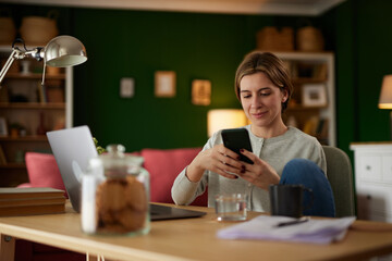 Attractive young woman text messaging on the phone at home office
