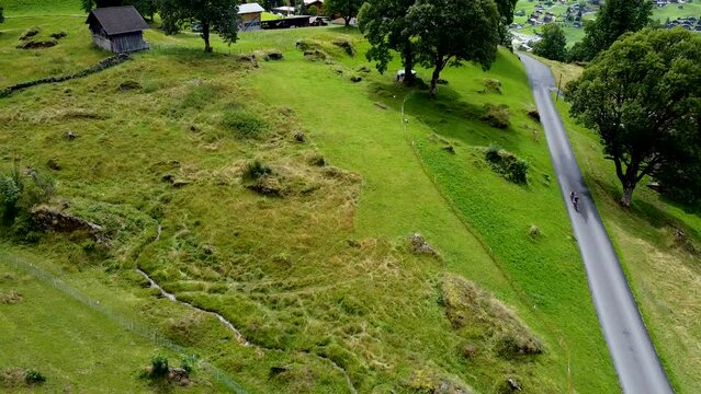 Cinematic aerial drone footage shot flying over Grindelwald landscape, pushing in over traditional houses and lush green picturesque meadows in Switzerland&rsquo;s Bernese Alps.