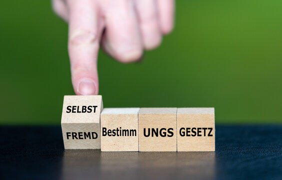Hand dreht Holzw&uuml;rfel und &auml;ndert den Ausdruck Fremdbestimmungsgesetz in Selbstbestimmungsgesetz.