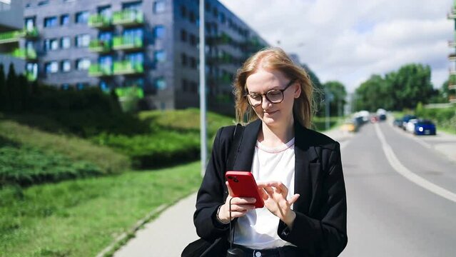 Smiling businesswoman using her phone outdoors. Small business entrepreneur looking at her mobile phone and smiling while communicating with her office colleagues. High quality 