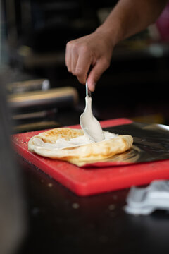 Malawach, a traditional Yemeni Jewish dish, being prepared at a food stall in Tel Aviv, Israel. It consists of flatbread made from puff pastry, topped here with creamy, white, fresh cheese.