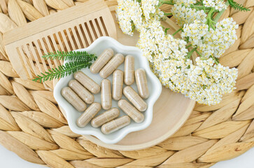 Small white bowl with food supplement capsules and yarrow flowers. Natural healthcare, herbal medicine, skincare and beauty treatment.